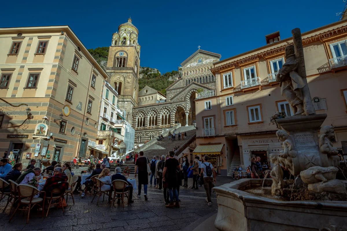 The striped facade and bell tower of Amalfi cathedral above the cafes of Piazza Duomo