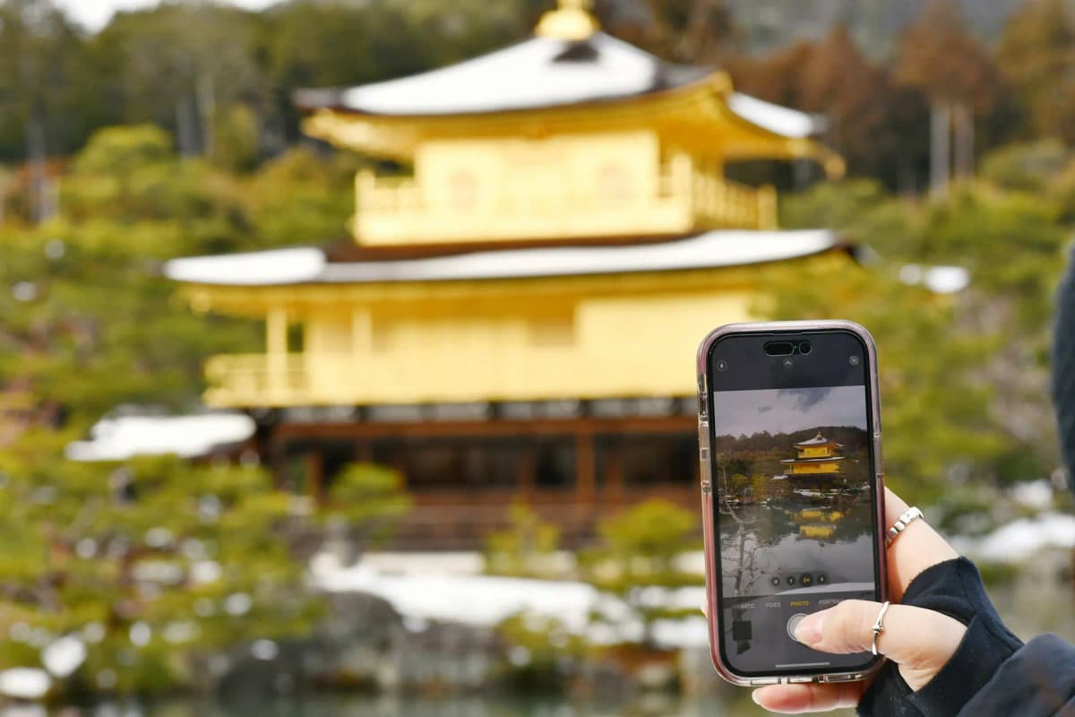 A traveller holding up a smartphone to photograph Kinkaku-ji, the Golden Pavilion in Kyoto