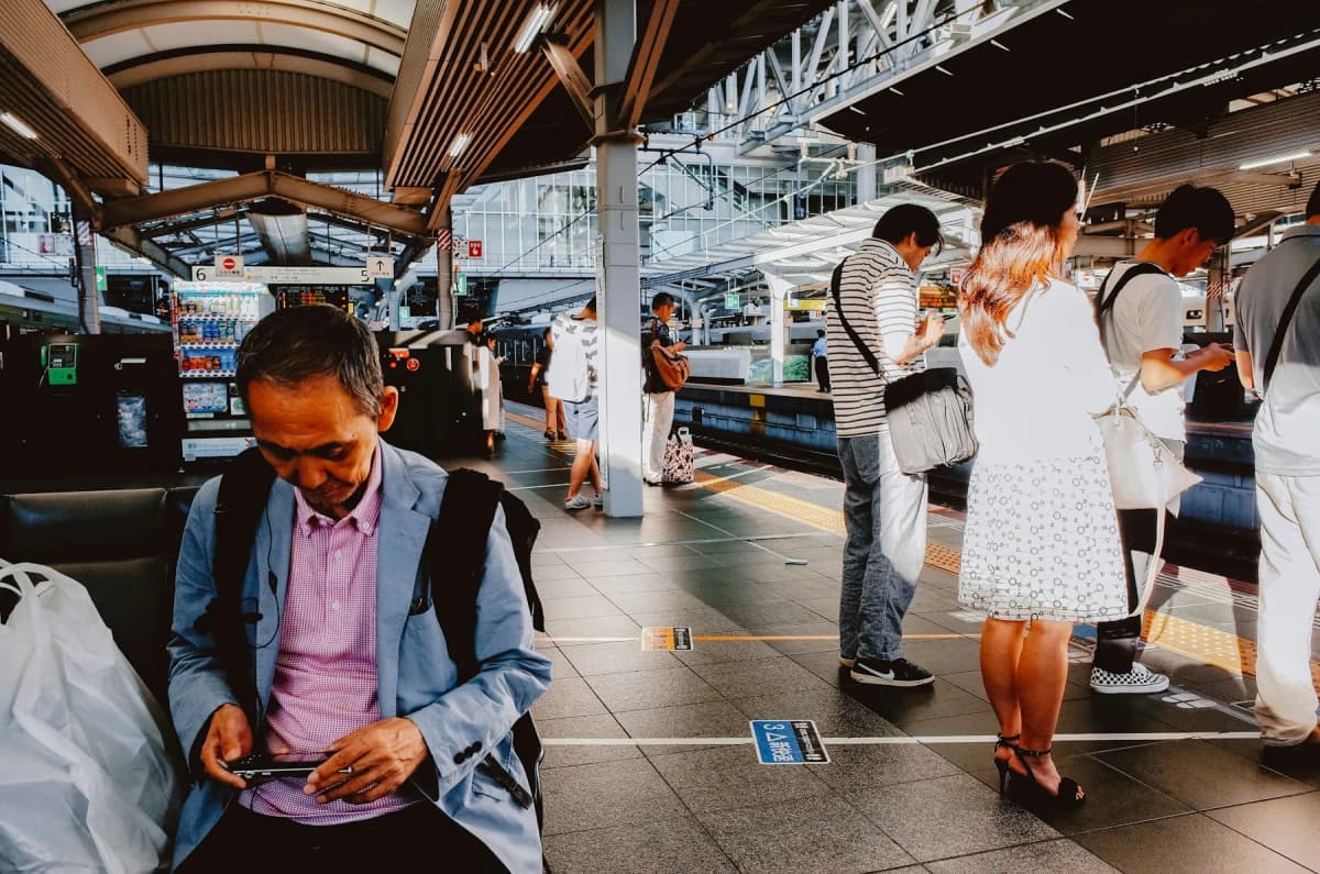 Passengers checking their phones while waiting on a train platform at a station in Japan