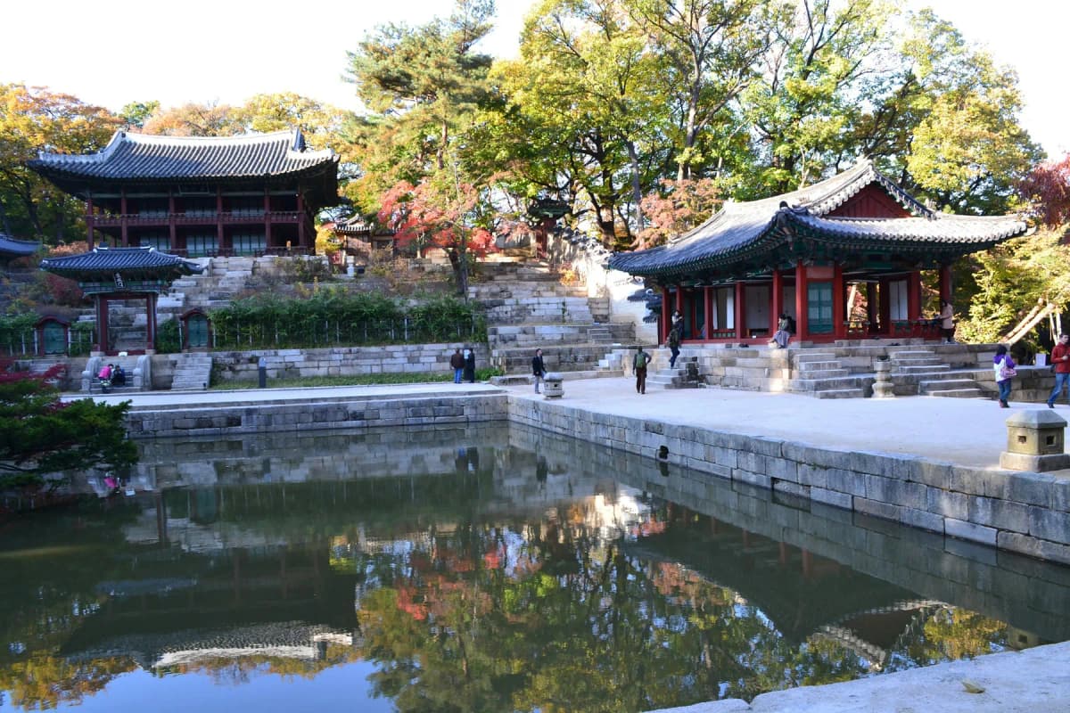 A traditional pavilion reflected in a pond surrounded by autumn trees in the Secret Garden of Changdeokgung
