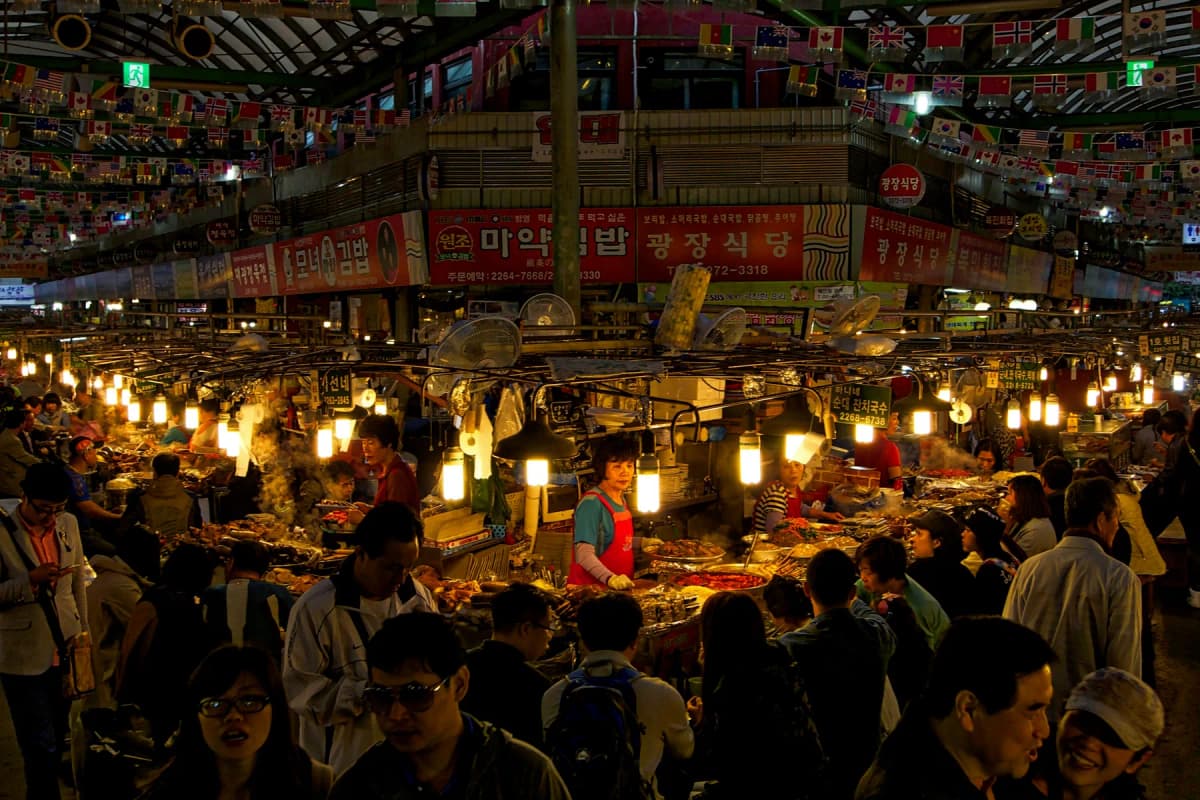 Diners and food stalls under the lights of a busy covered food market in Seoul