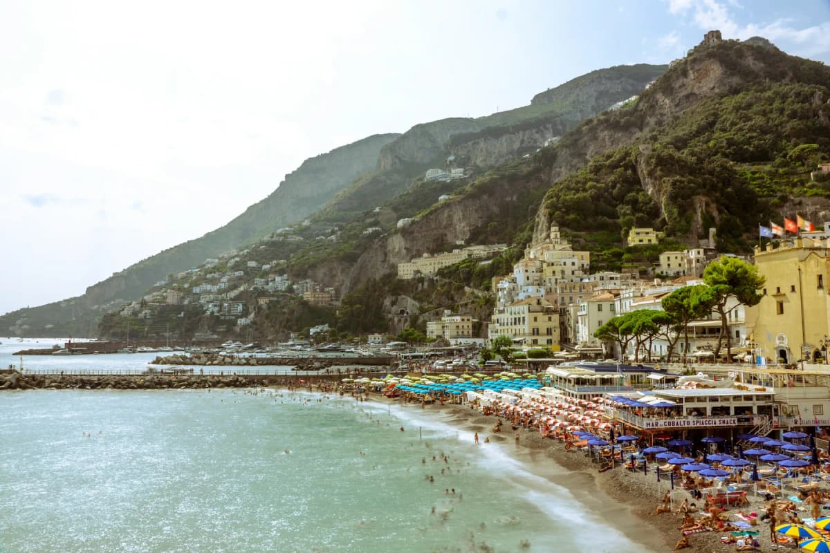 A crowded Amalfi Coast beach in summer with rows of umbrellas and swimmers in the sea