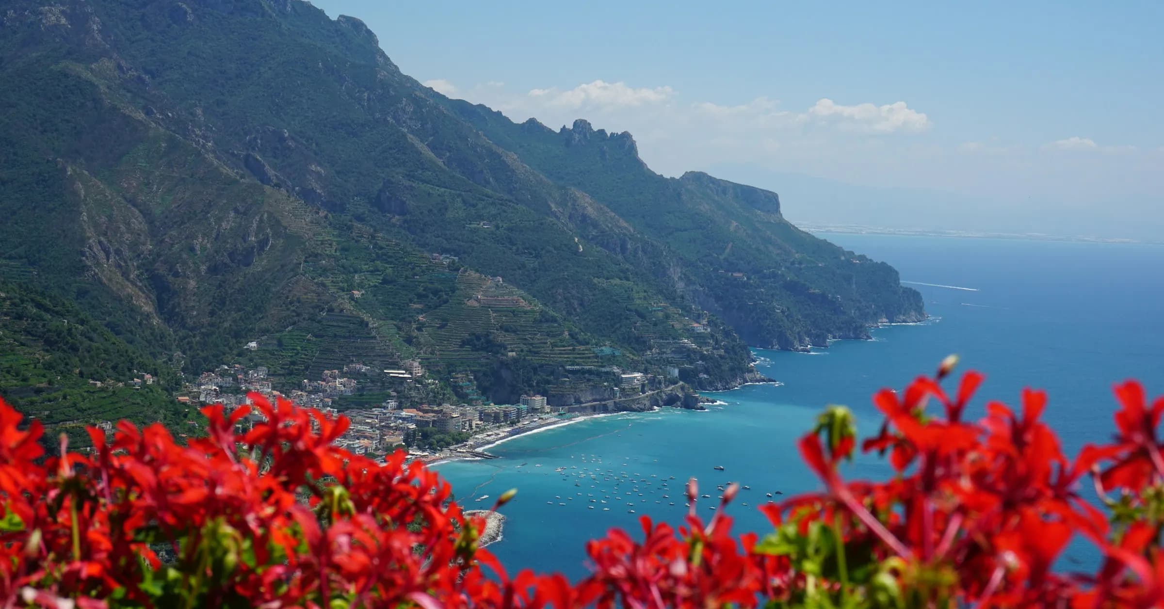 Best time to visit Amalfi Coast: red geraniums on a terrace overlooking the coastline and the sea in summer