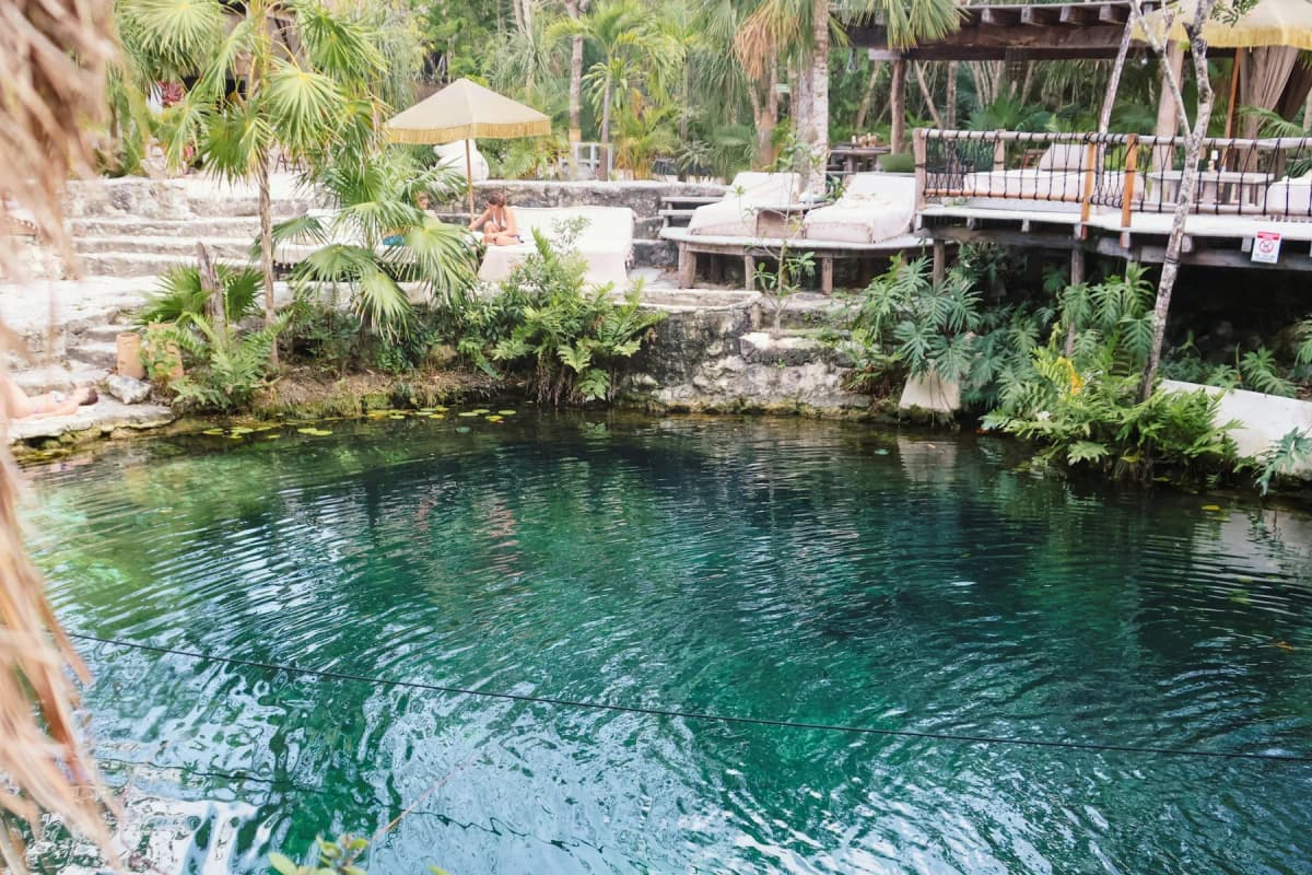 Swimmers in a cenote with loungers and umbrellas at its edge, near Tulum