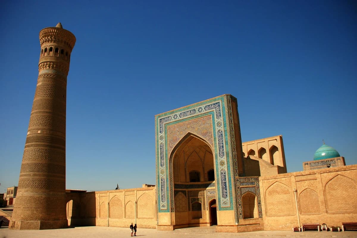 The Kalyan Minaret beside a tiled portal on Po-i-Kalyan square in Bukhara, under a deep blue sky