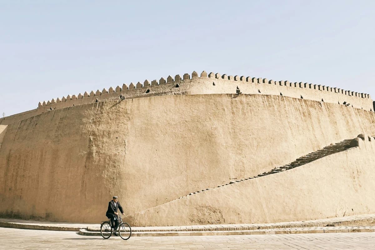 The mud-brick walls of Itchan Kala in Khiva, with a cyclist passing below