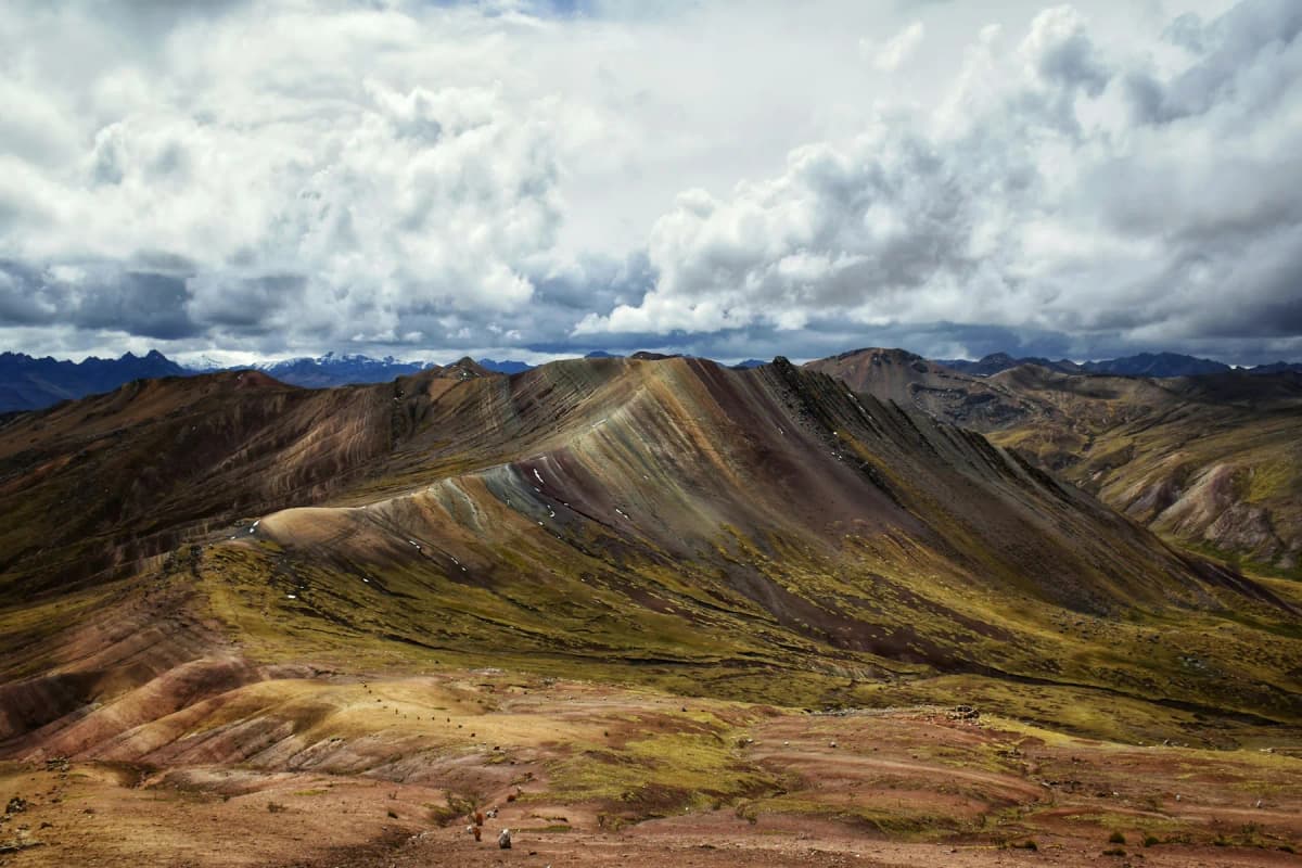 Striped red, green and ochre ridges at Palccoyo under heavy clouds