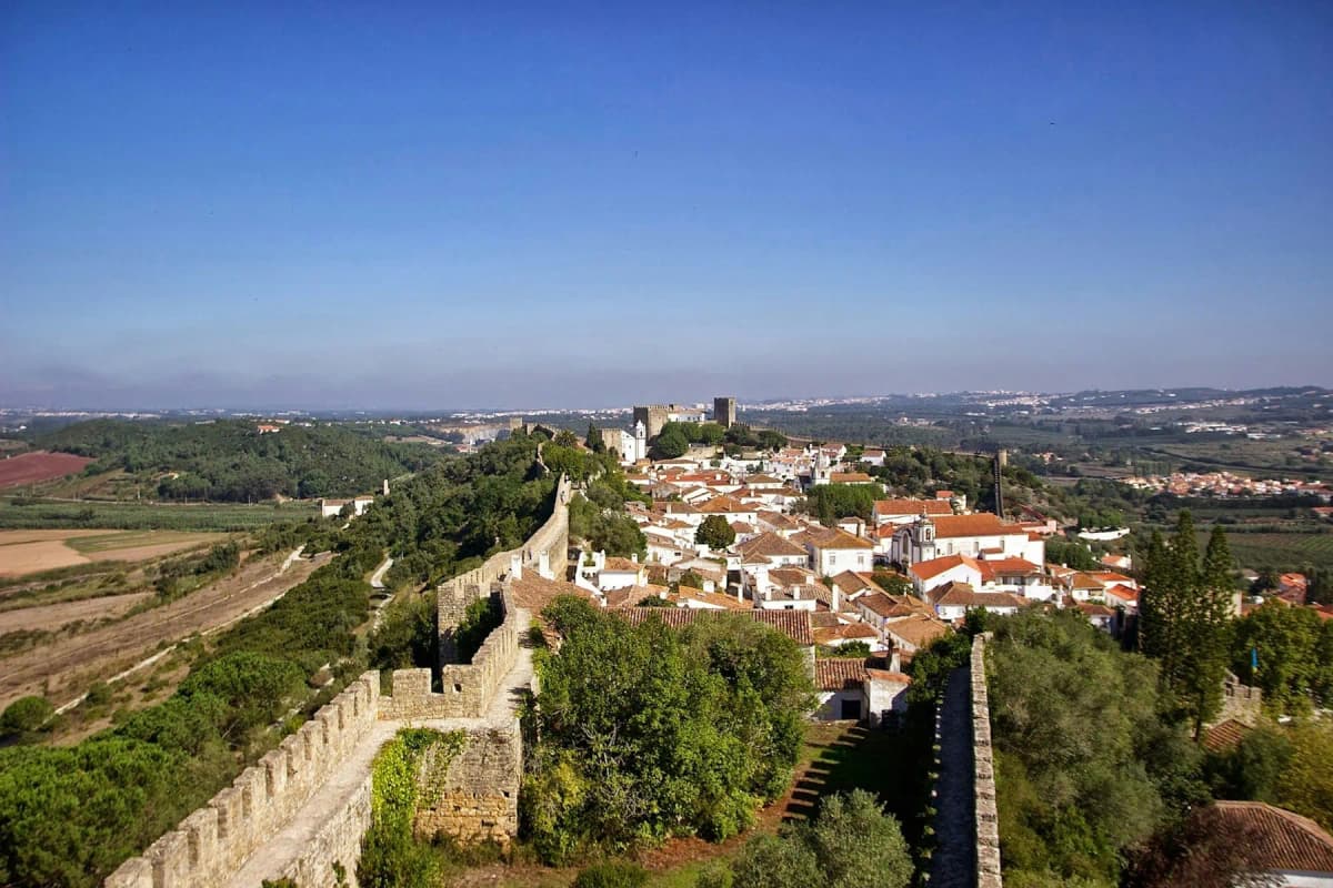 The medieval walls of Óbidos curving around whitewashed houses with terracotta roofs
