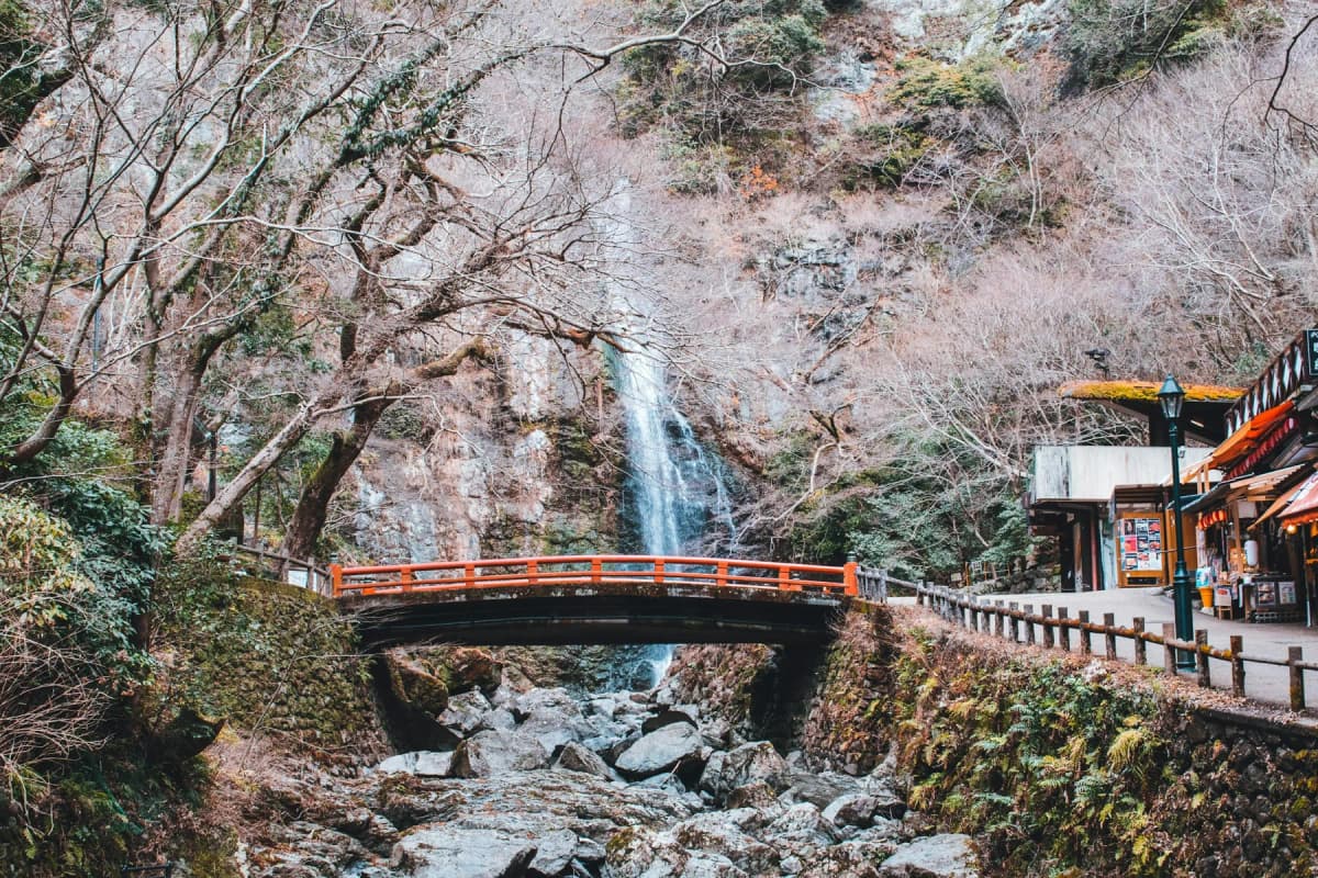 An orange bridge in front of Minoh waterfall in a wooded valley near Osaka