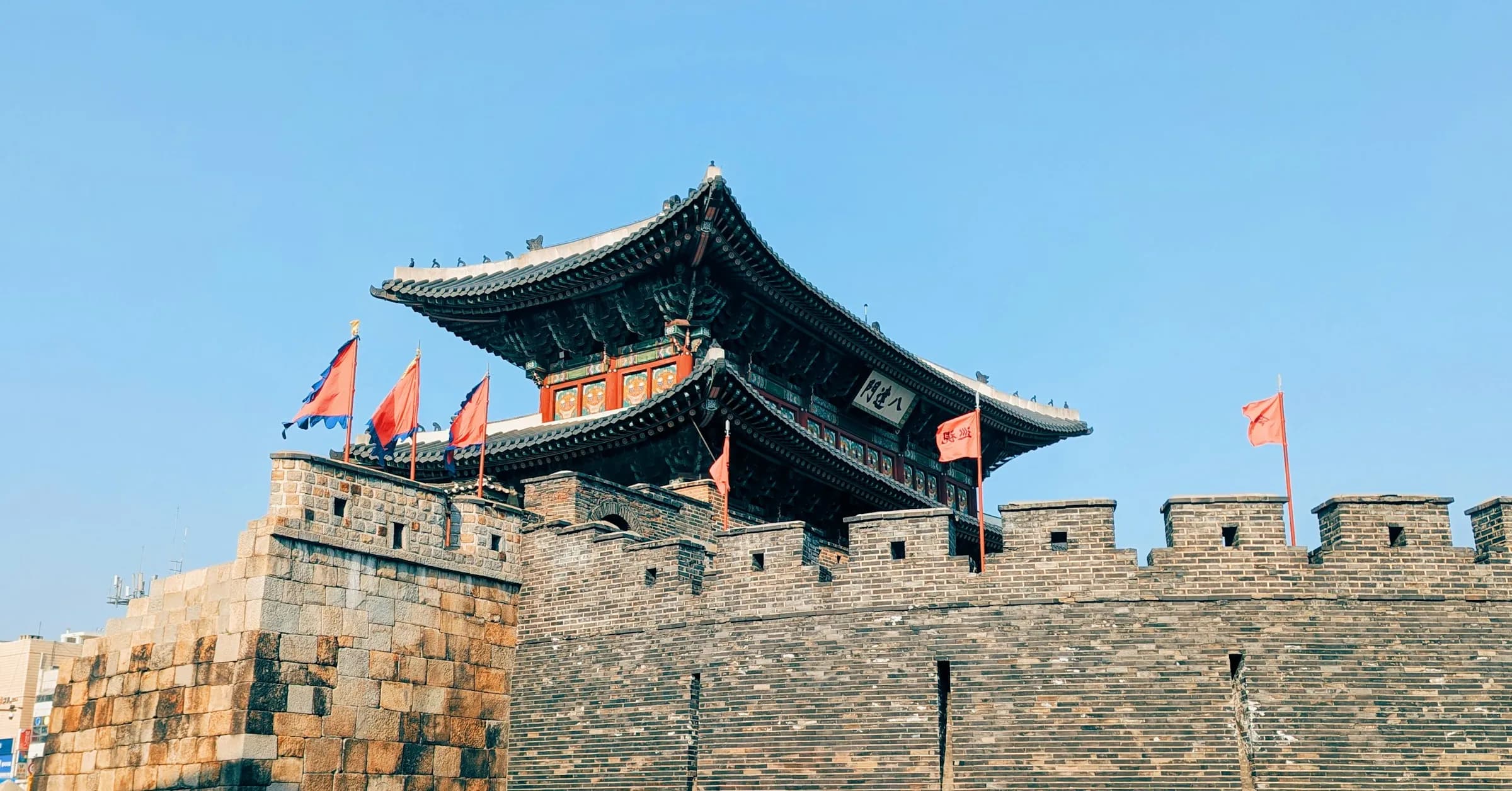 Day trips from Seoul: a gate of Suwon's Hwaseong Fortress with red flags on the walls under a blue sky