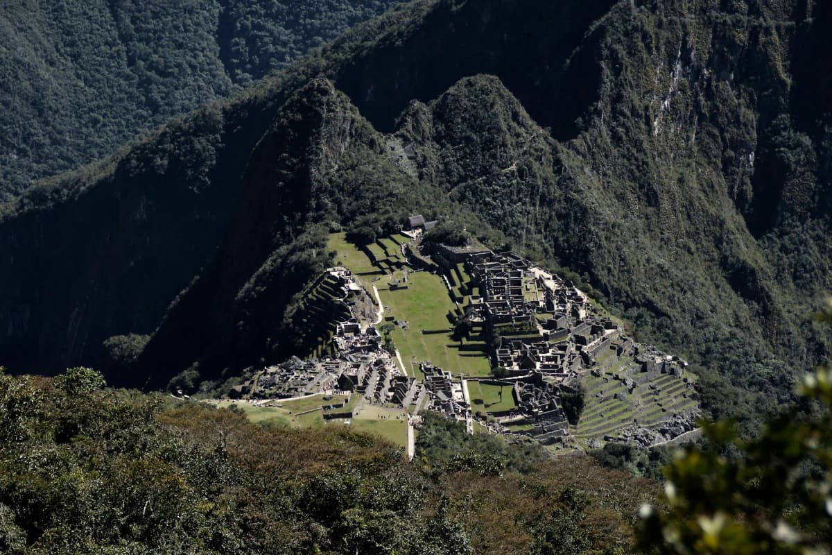 Machu Picchu seen from high above, on a ridge between steep, forested mountains