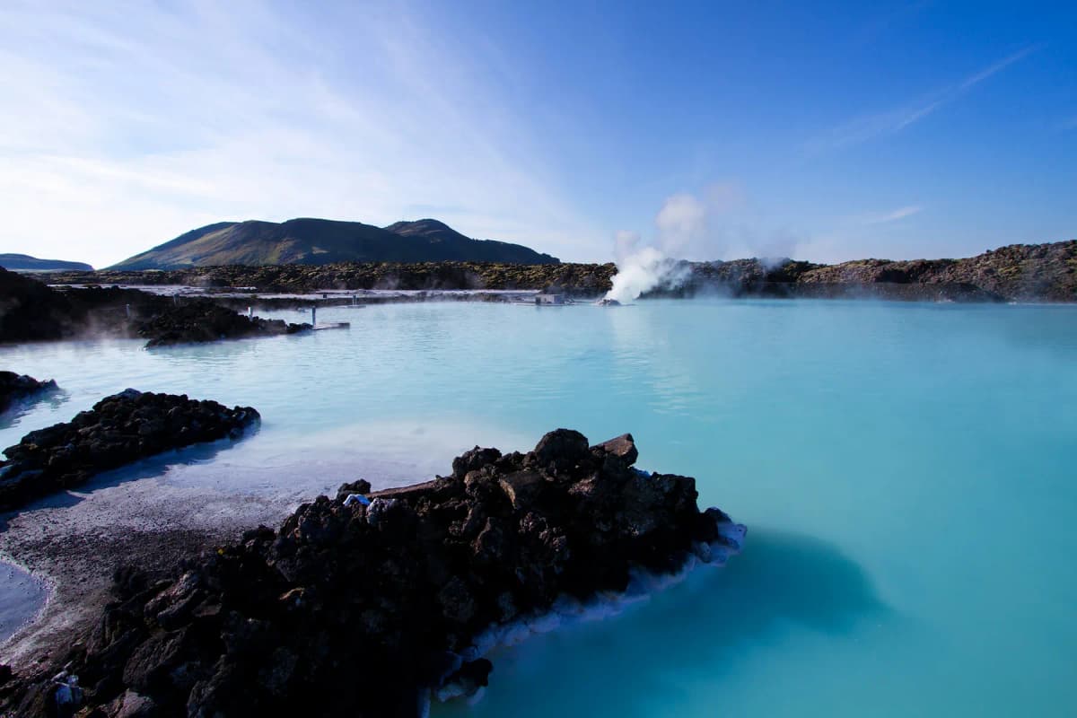The milky blue water of the Blue Lagoon geothermal spa with dark lava rocks and steam rising in the distance