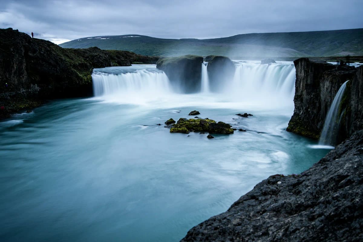 Goðafoss waterfall pouring over a wide horseshoe-shaped rock ledge into a blue-green river