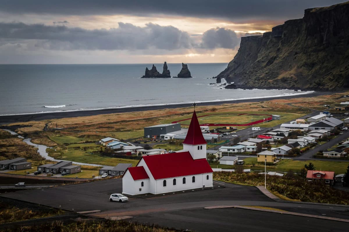 The red-roofed church above Vík with the Reynisdrangar sea stacks offshore and cliffs on the right