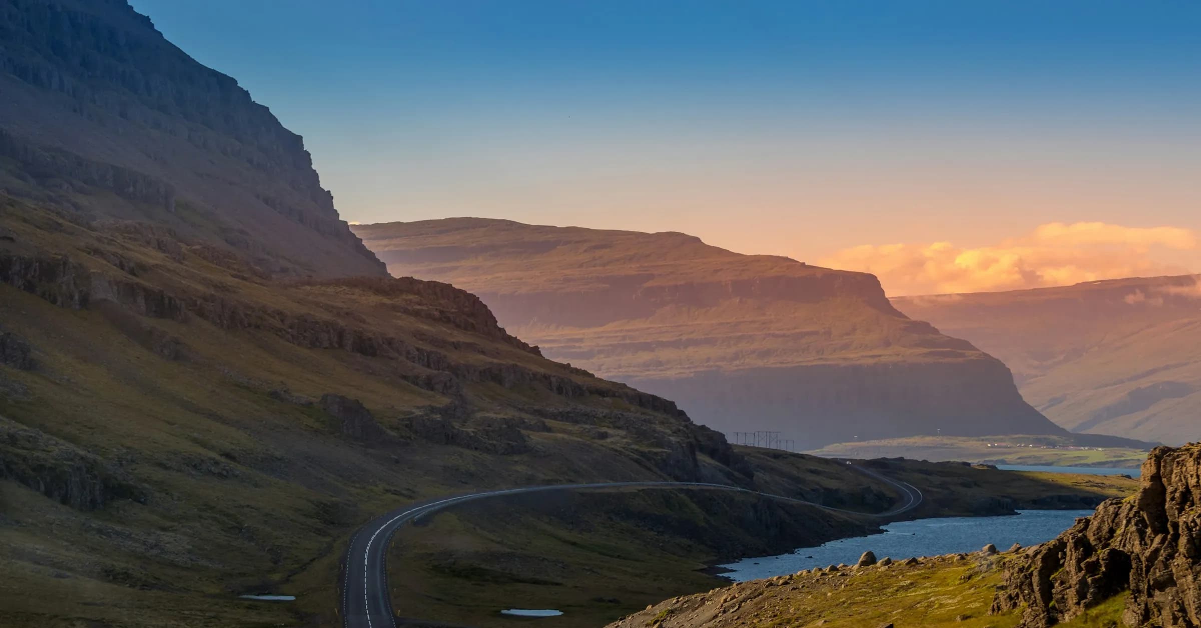 Iceland itinerary: a road winding along a fjord beneath steep mountains at sunset