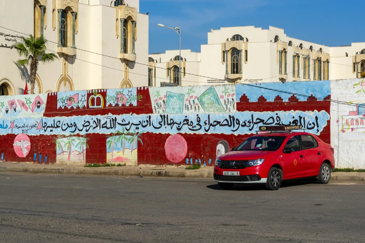 A red petit taxi parked in front of a painted wall and white buildings in Casablanca