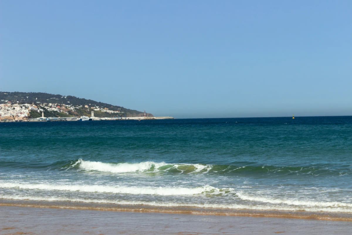 Waves breaking on a sandy beach near Tangier with the city on the headland in the distance