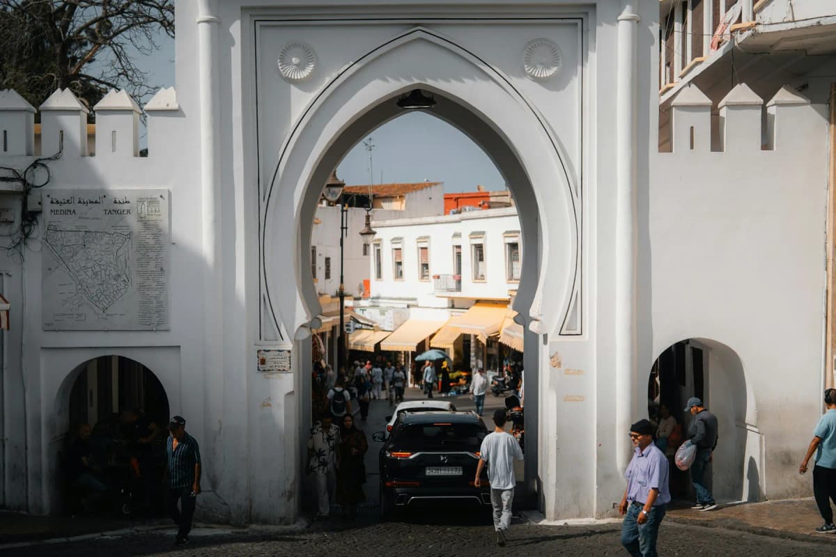 Is Tangier safe: people and cars passing through a white horseshoe-arched gate into the medina of Tangier