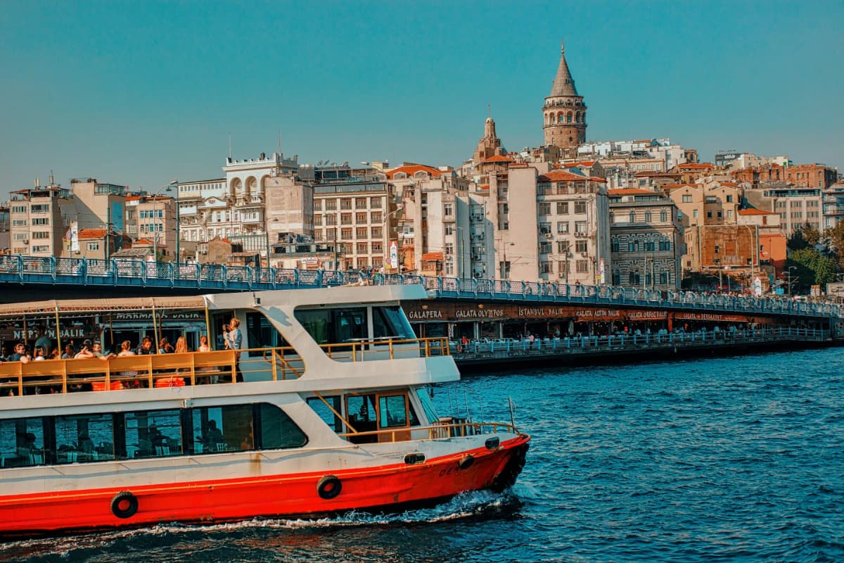 A red and white Istanbul ferry crossing in front of Galata Tower