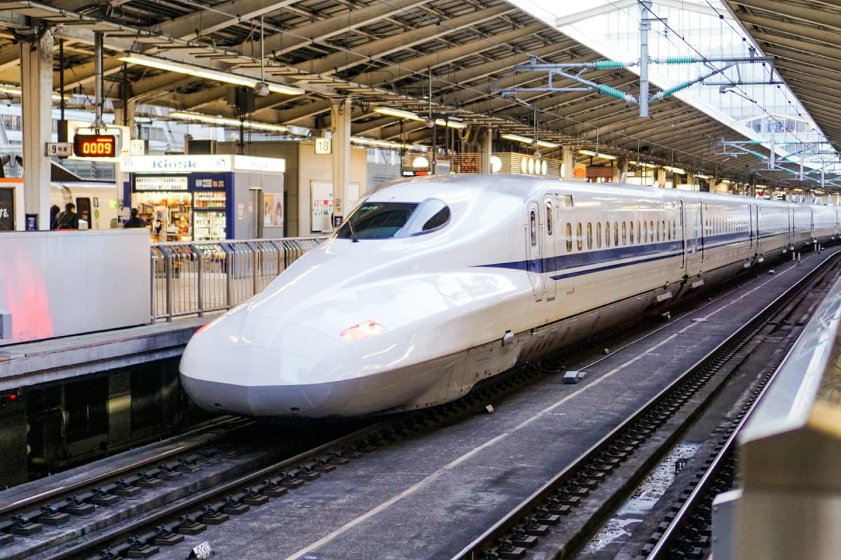 A white Shinkansen bullet train arriving at a station platform in Japan