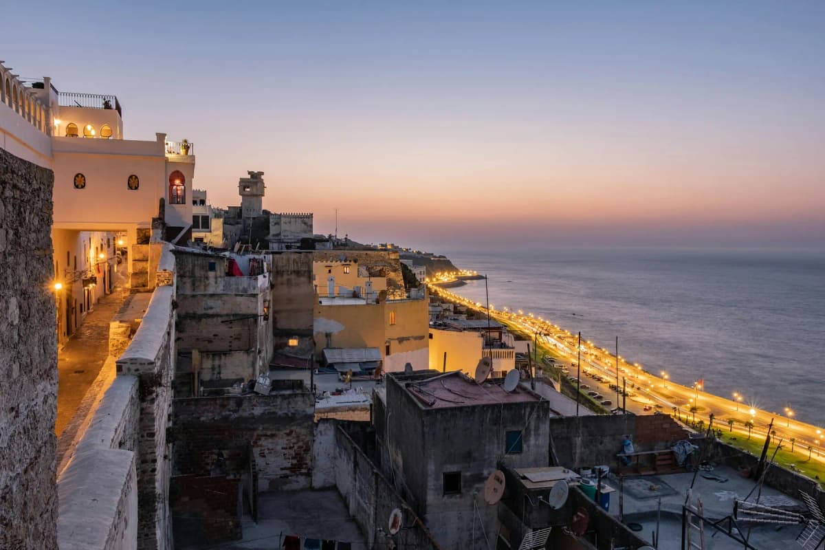 The medina of Tangier at dusk, with whitewashed houses above the seafront and the Strait of Gibraltar