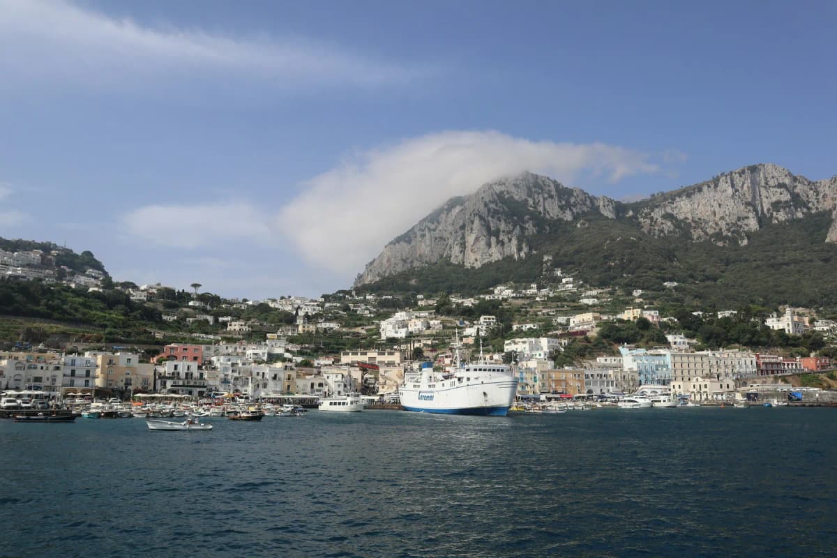 A large white conventional ferry in a harbour below a rocky mountain