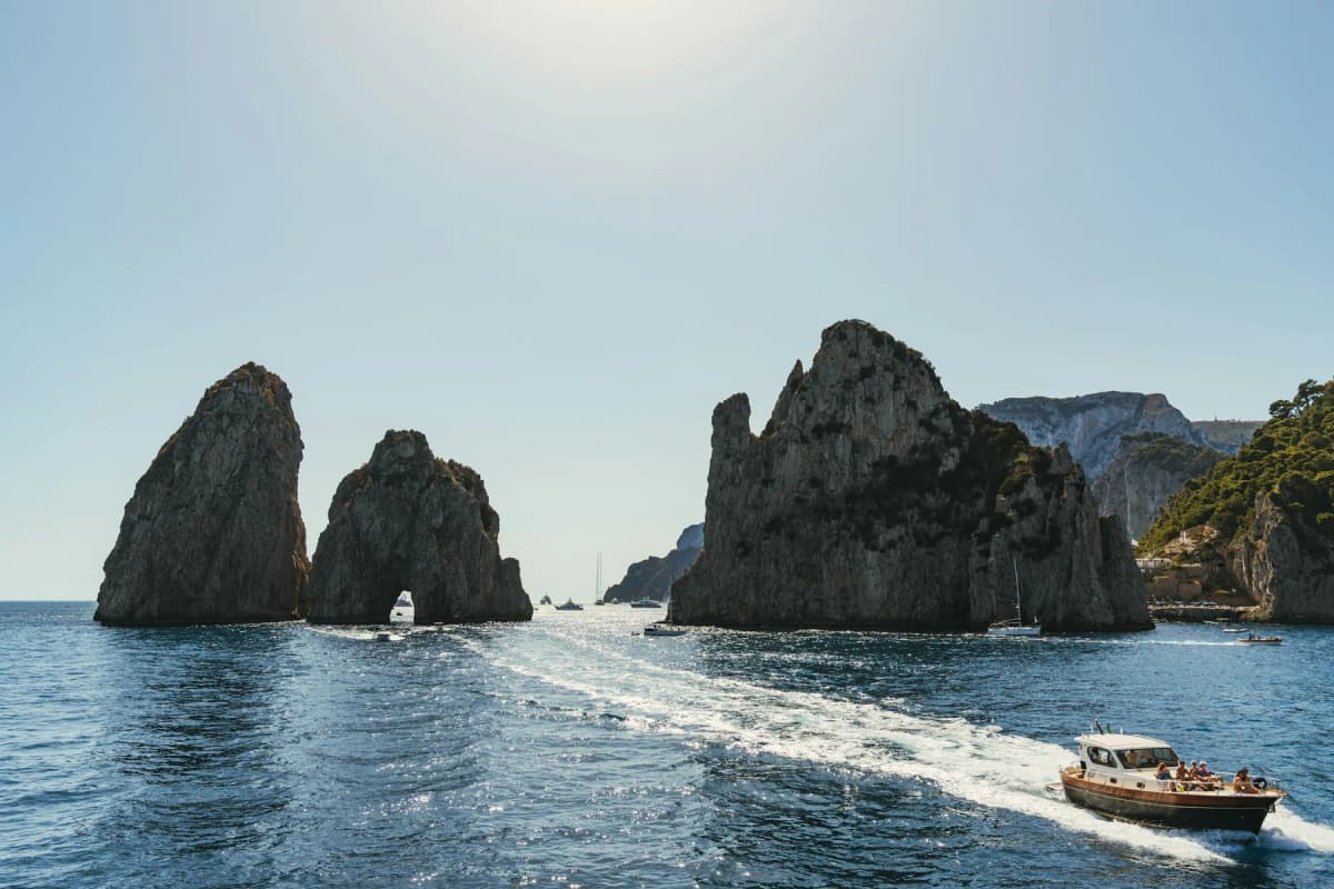 Small boats passing the Faraglioni sea stacks off the coast of Capri