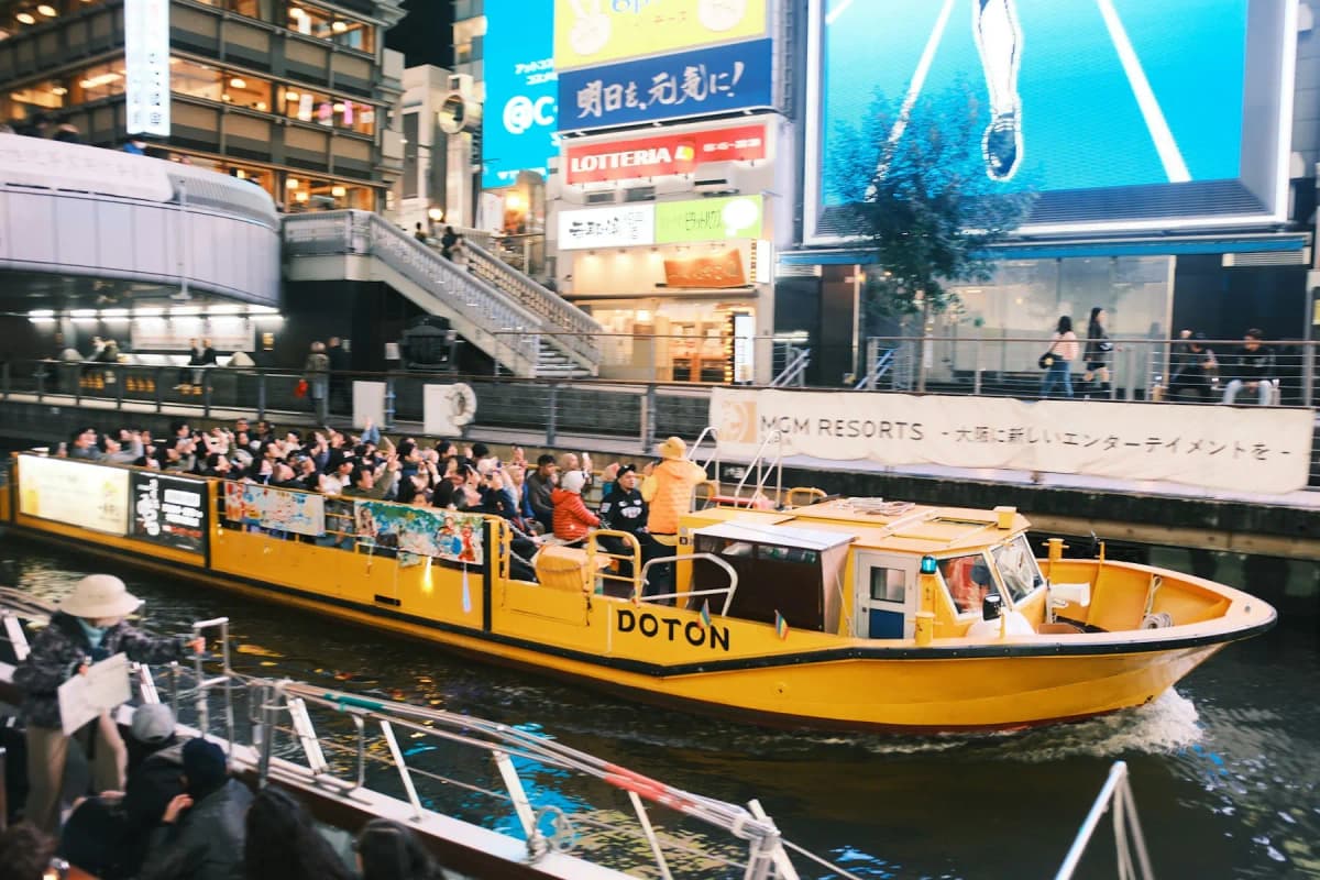 A yellow sightseeing boat full of passengers on the Dotonbori canal in Osaka