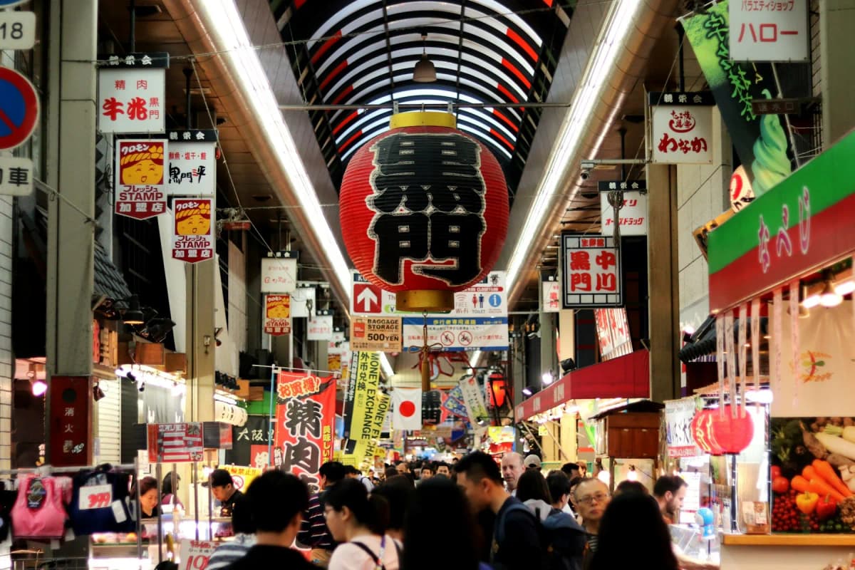 Shoppers under the red lantern and covered arcade of Kuromon Market in Osaka