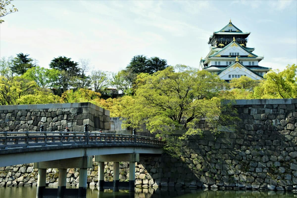 The main tower of Osaka Castle rising above stone walls, a bridge and green trees