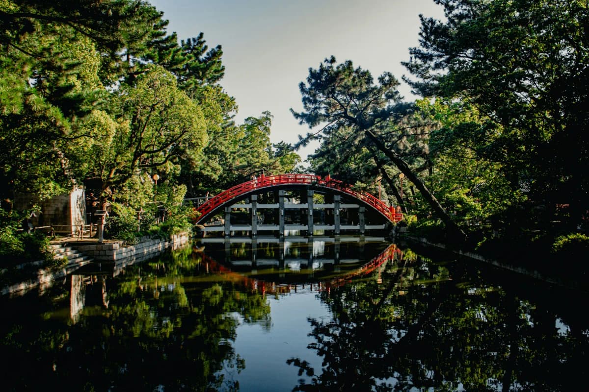 The red arched Sorihashi bridge reflected in a pond among pine trees at Sumiyoshi Taisha
