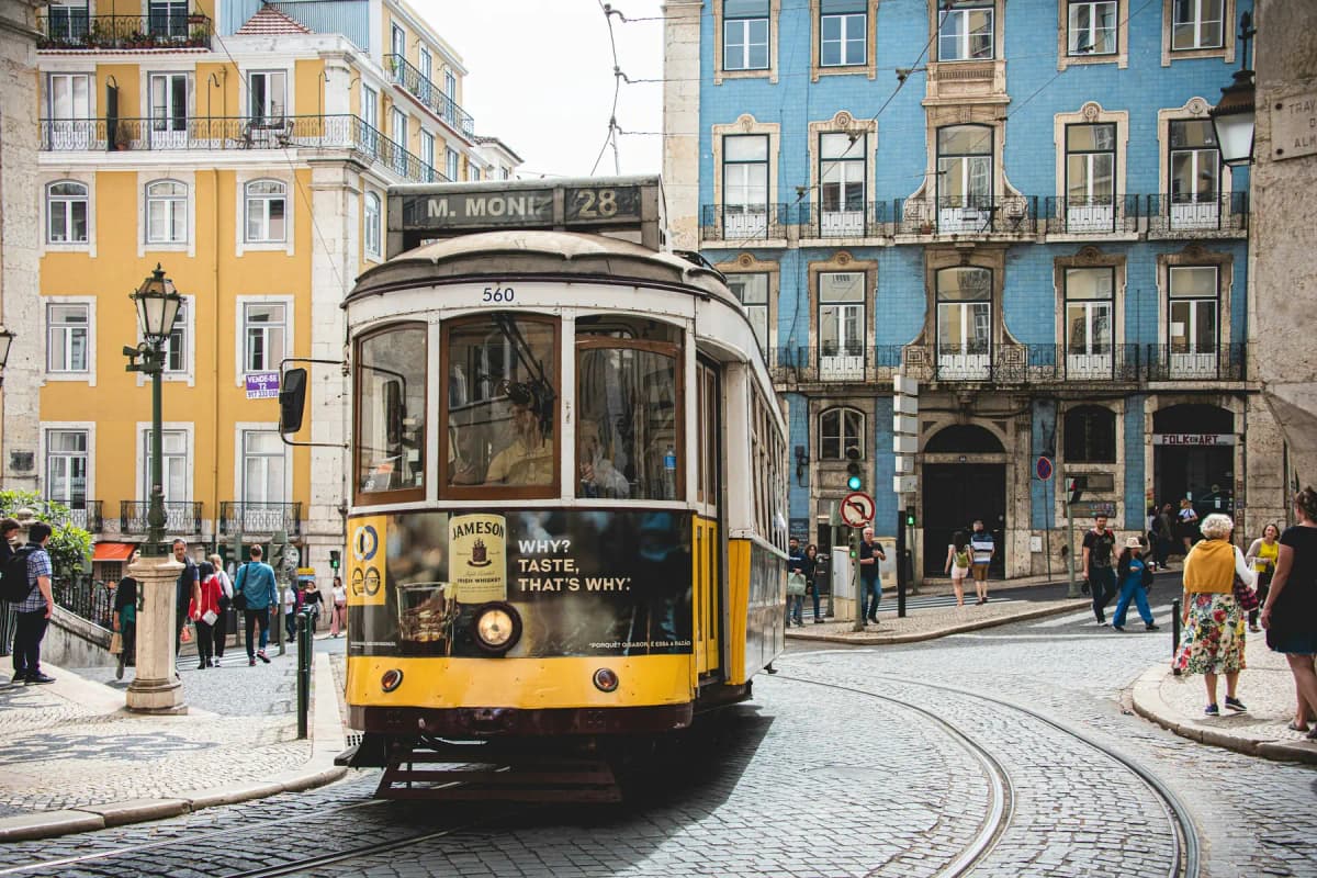 A yellow Lisbon tram passing blue-tiled buildings on a cobbled street in the city centre