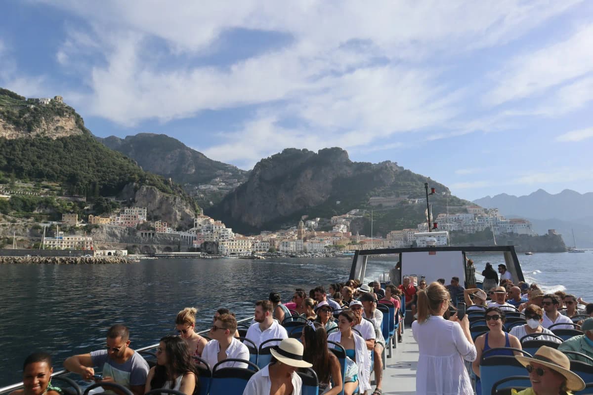 Passengers on the open top deck of a ferry approaching a town on the Amalfi Coast