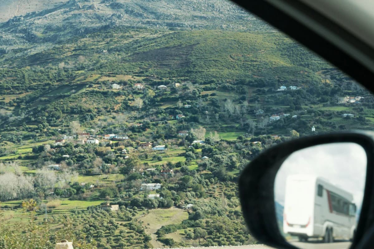 Green terraced hills of the Rif seen from a car, with a bus in the wing mirror, on the road from Tangier to Chefchaouen