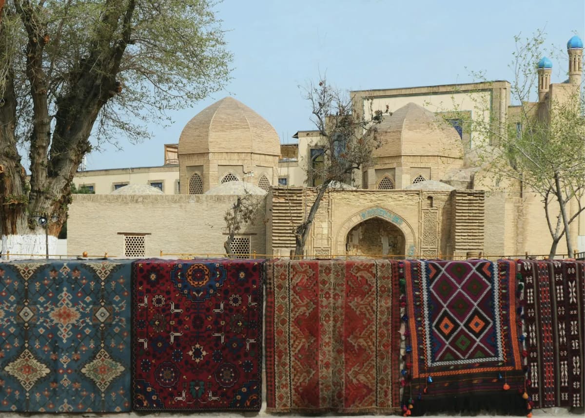 Things to do in Bukhara: handwoven carpets hung on a wall in front of a domed madrasah in the old town