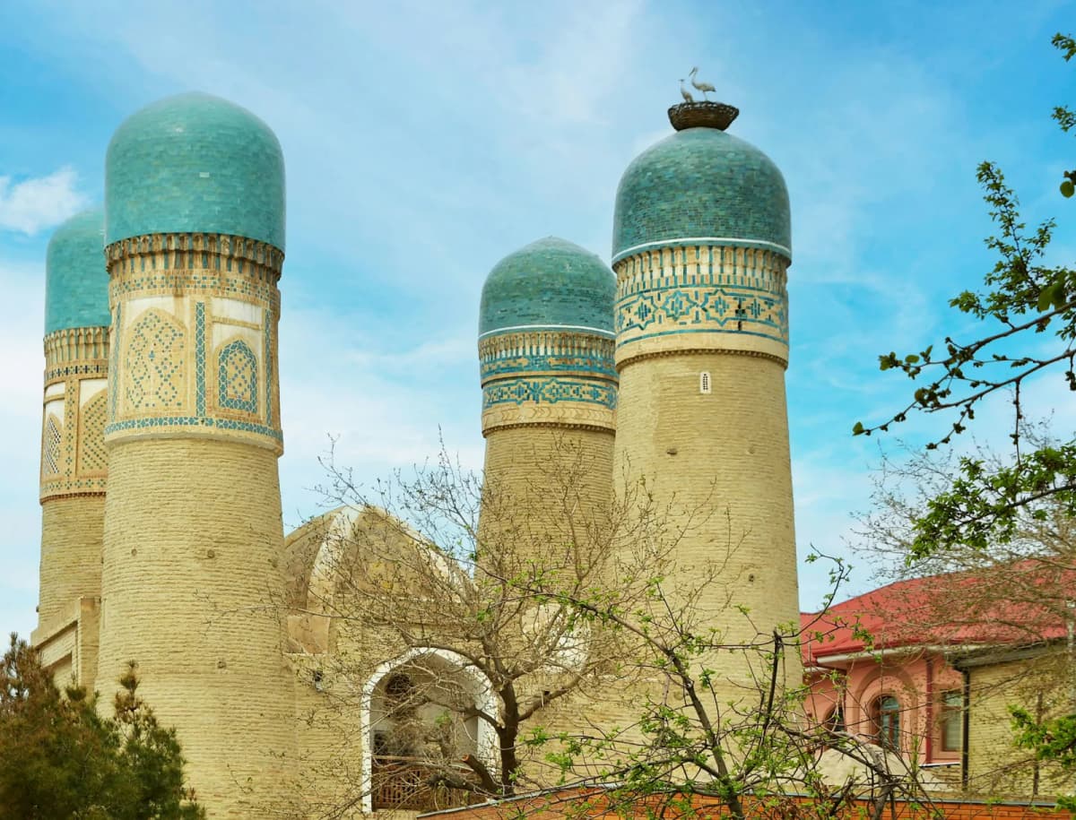 Things to do in Bukhara: the four blue-domed towers of Chor Minor against a blue sky, with trees in front