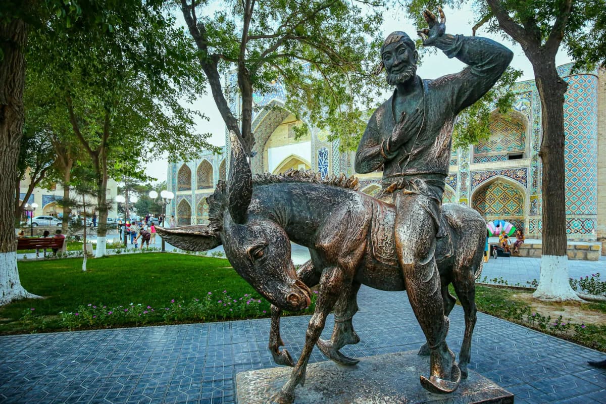 Things to do in Bukhara: the bronze statue of Khodja Nasreddin on his donkey by Lyabi-Hauz, with a madrasah behind the trees