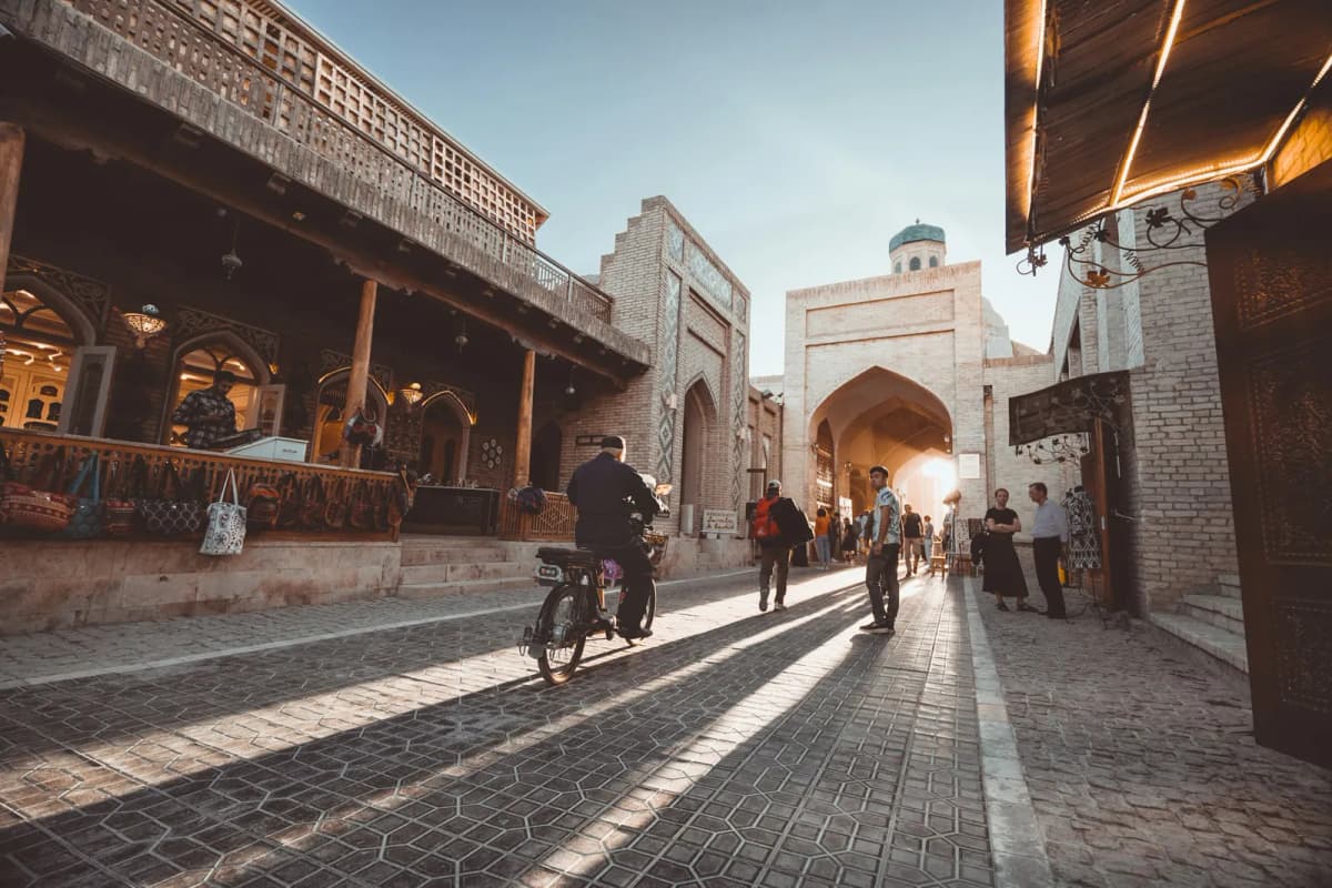 Things to do in Bukhara: a late-afternoon lane in the old town with a cyclist, shopfronts and a domed gate at the end