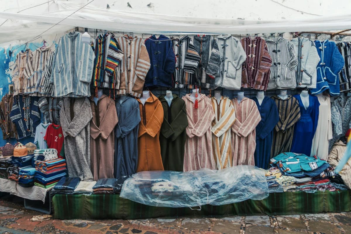 Wool djellabas and woven textiles hanging outside a shop on a blue lane in Chefchaouen