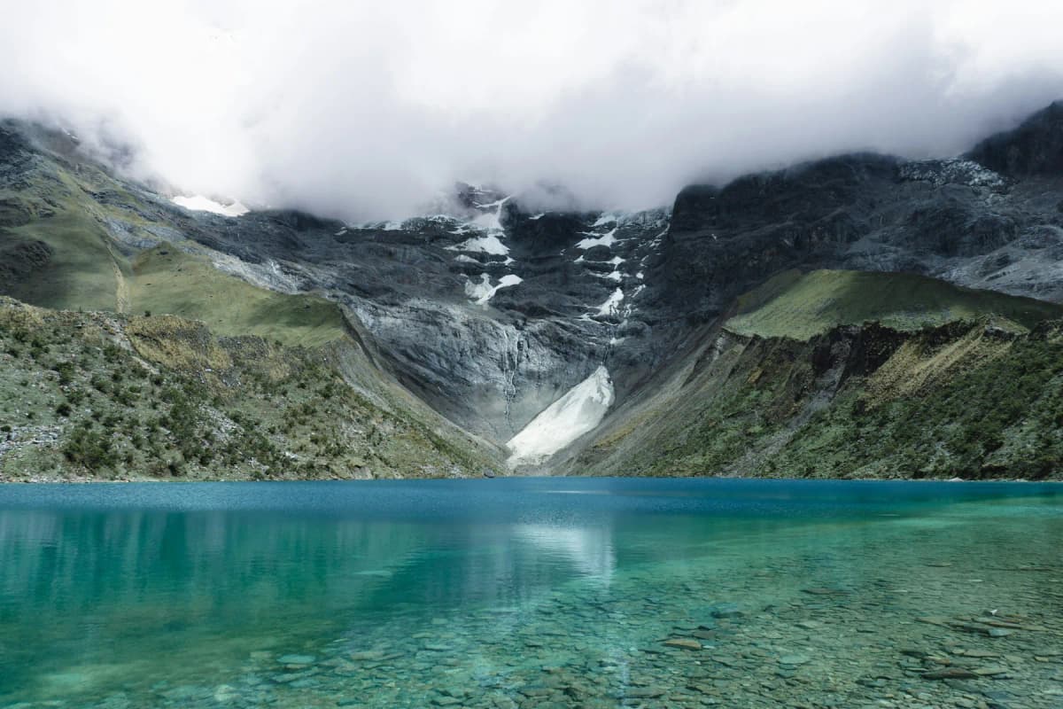 The turquoise water of Humantay Lake beneath steep, cloud-covered glacier slopes