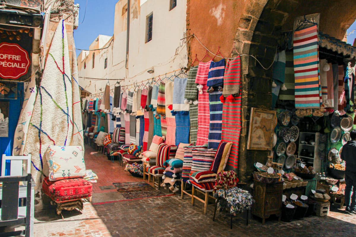A lane in the Essaouira medina lined with striped rugs, blankets and baskets for sale