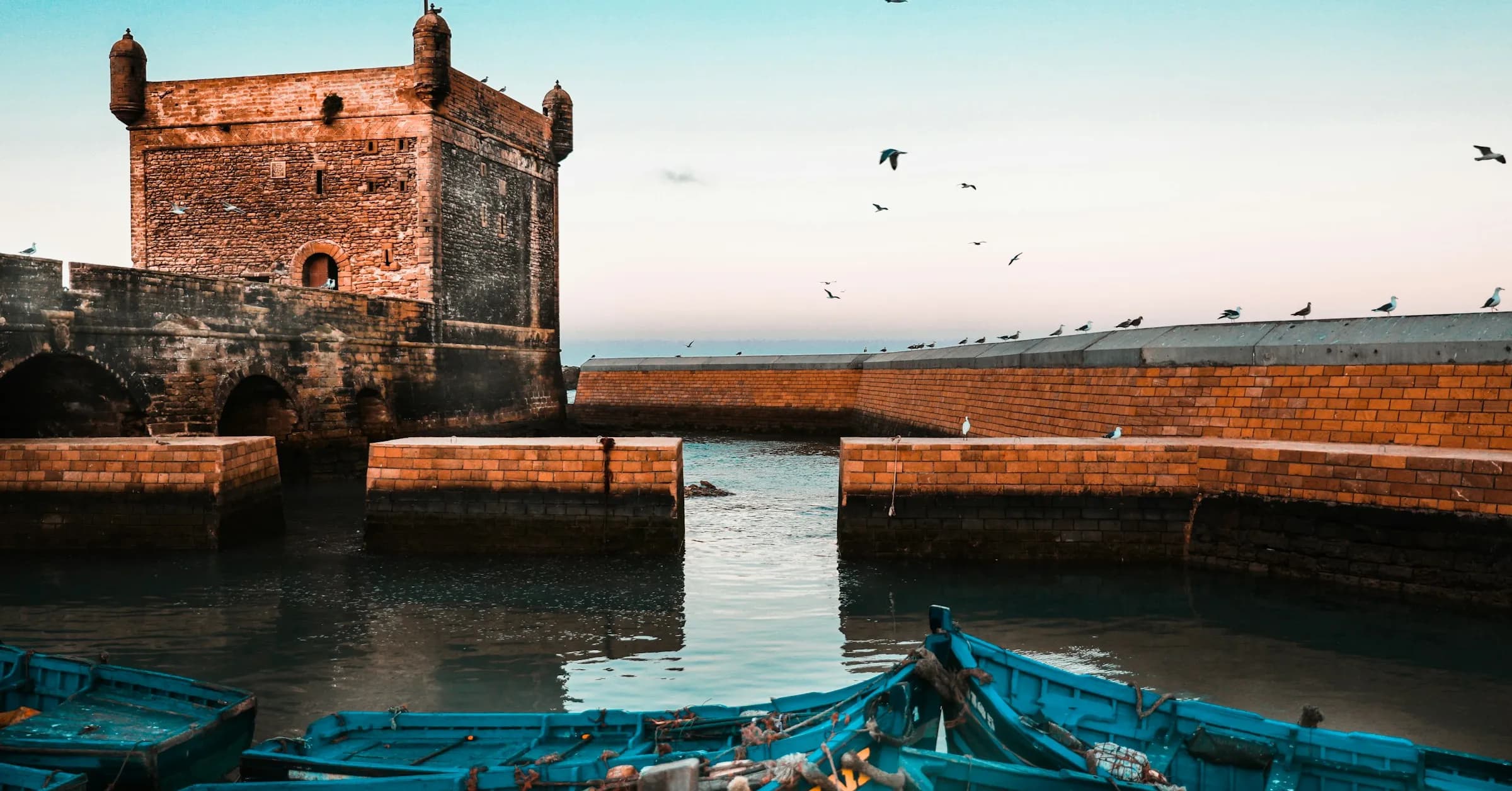 Things to do in Essaouira: the stone tower of the Skala du Port above blue fishing boats in the harbour