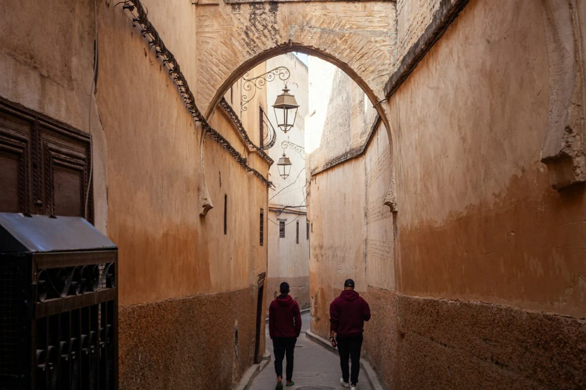 Things to do in Fes: two people walking under an arch in a narrow lane of the Fes el-Bali medina