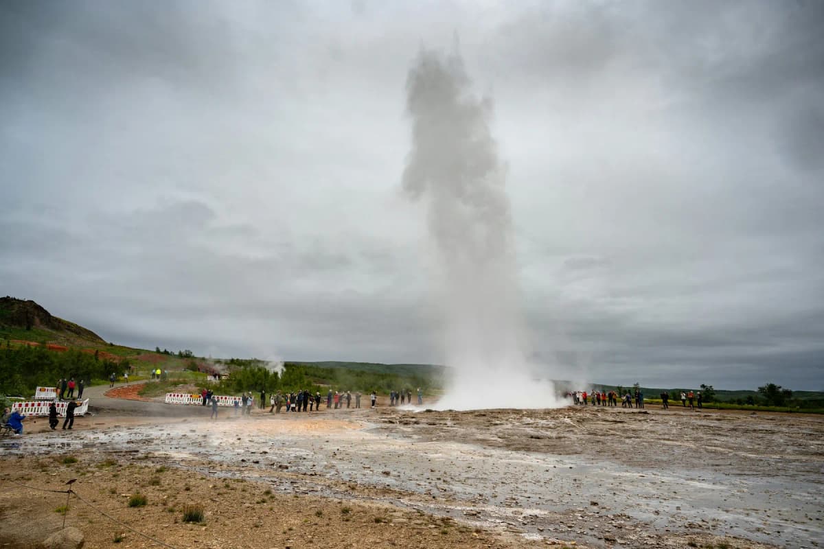 Strokkur geyser erupting in the Haukadalur geothermal area, with visitors watching from behind the rope line