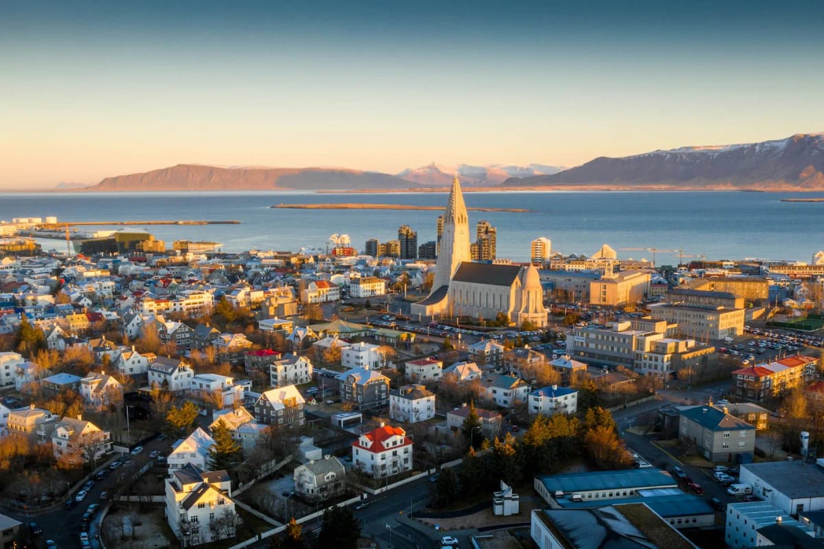 Aerial view of Reykjavik at sunset, with Hallgrímskirkja church rising above the colourful rooftops and the mountains across the bay