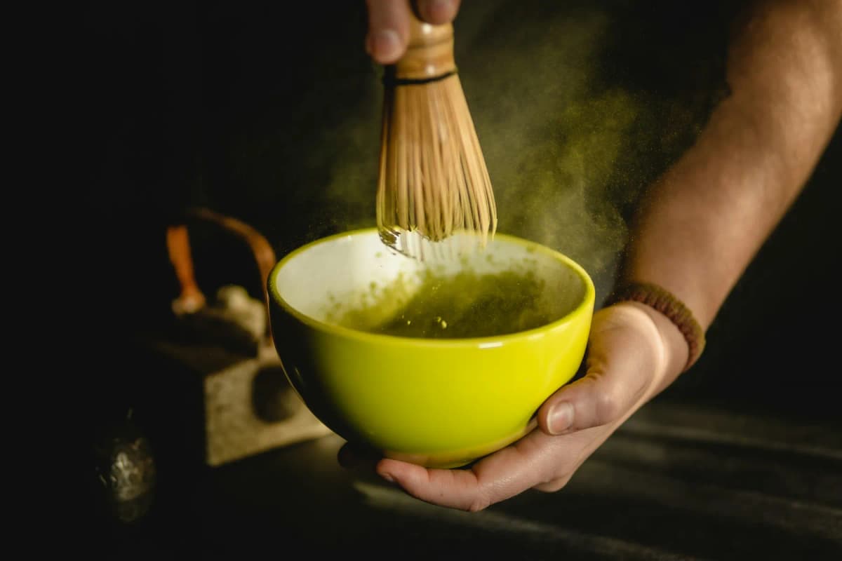 A hand whisking bright green matcha tea in a bowl during a tea ceremony