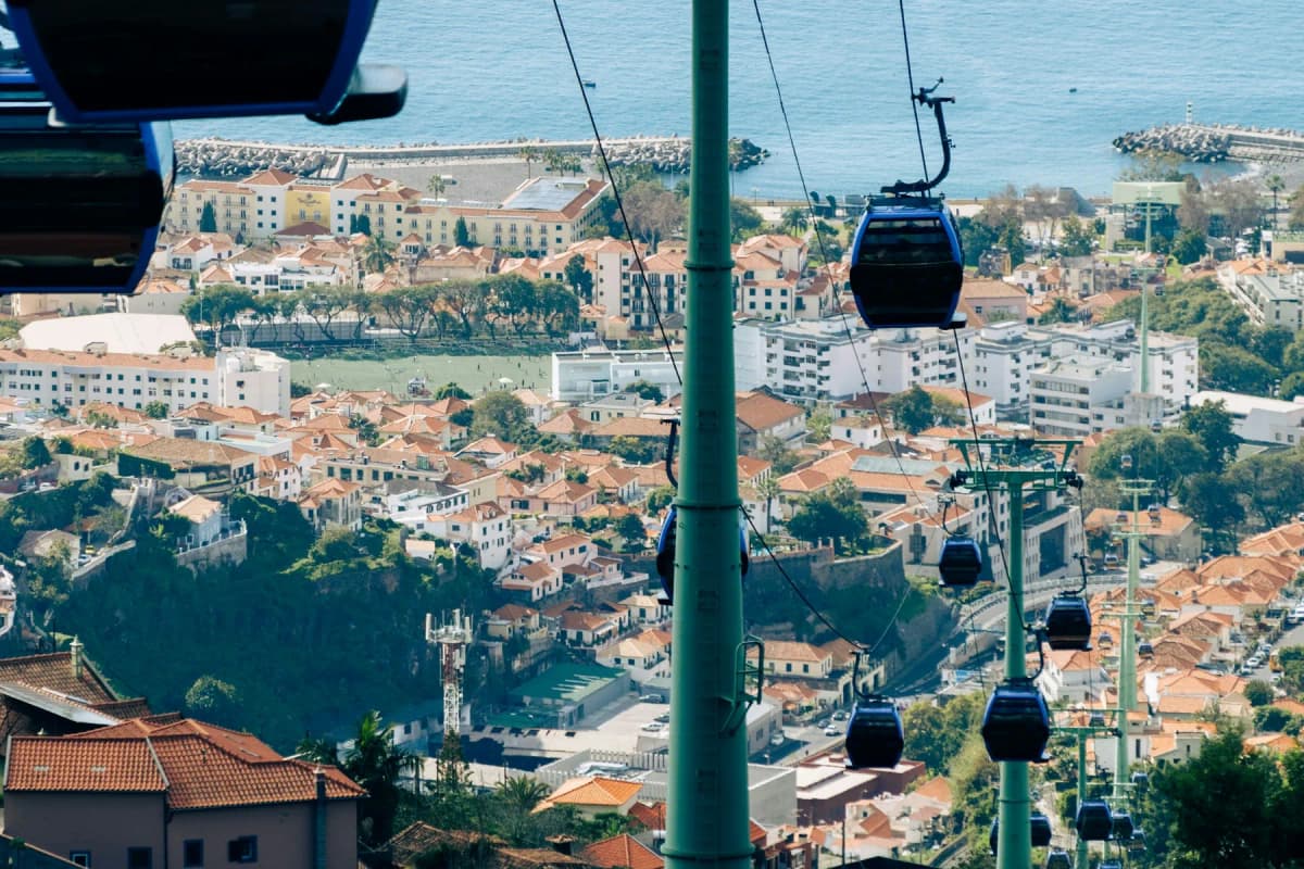 Cable cars climbing above the red rooftops of Funchal, with the harbour and the Atlantic behind