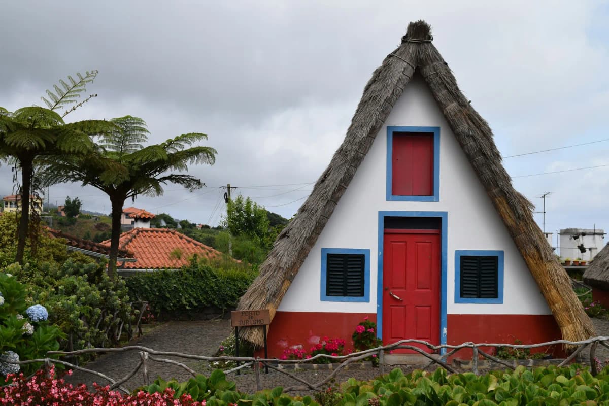 A traditional triangular thatched house with a red door and blue trim in Santana, Madeira