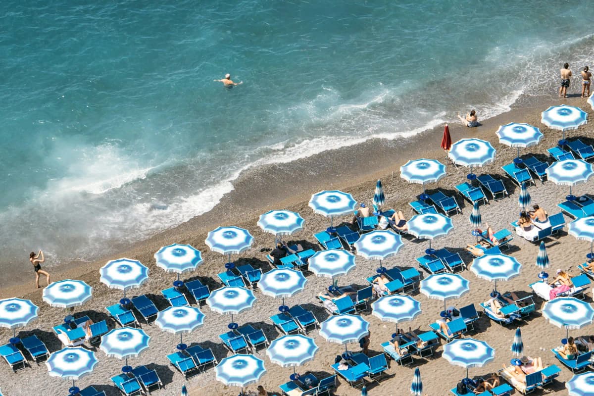 Blue and white striped beach umbrellas and sunbeds on a pebble beach beside clear water