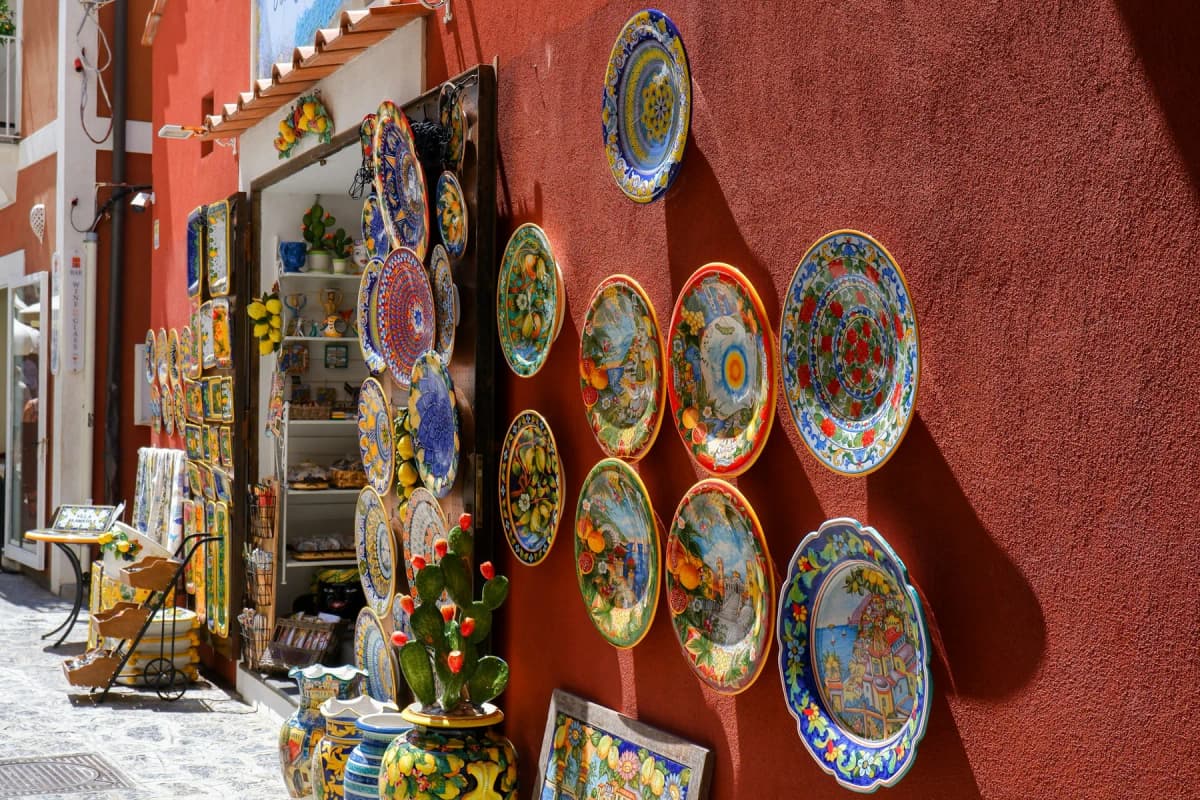 Hand-painted ceramic plates displayed on a red wall outside a shop on the Amalfi Coast